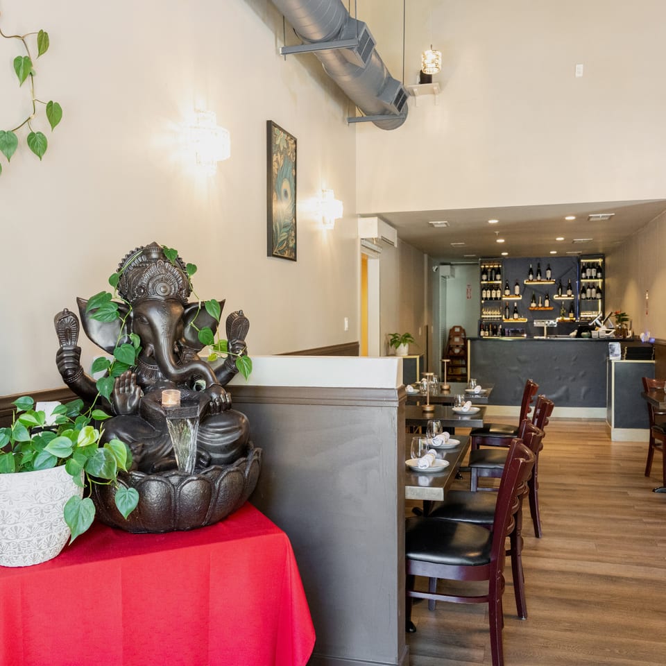 Restaurant interior with a Ganesha statue, dining tables, and a bar area with wine bottles.
