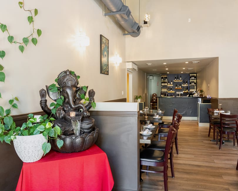 Restaurant interior with a Ganesha statue, dining tables, and a bar area with wine bottles.