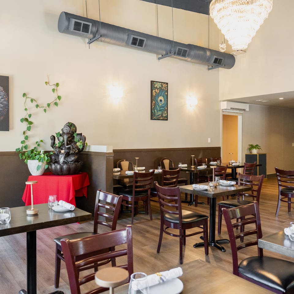 A restaurant dining room with dark wood tables, chairs, and a Ganesha statue with a water feature.
