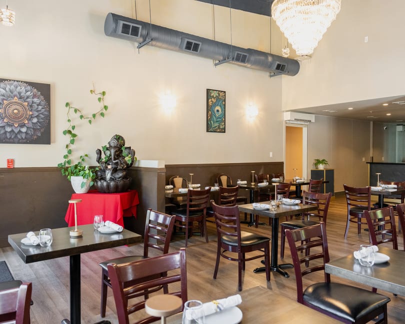 A restaurant dining room with dark wood tables, chairs, and a Ganesha statue with a water feature.