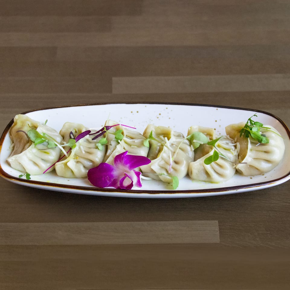 A white rectangular plate of dumplings garnished with microgreens and a purple orchid.