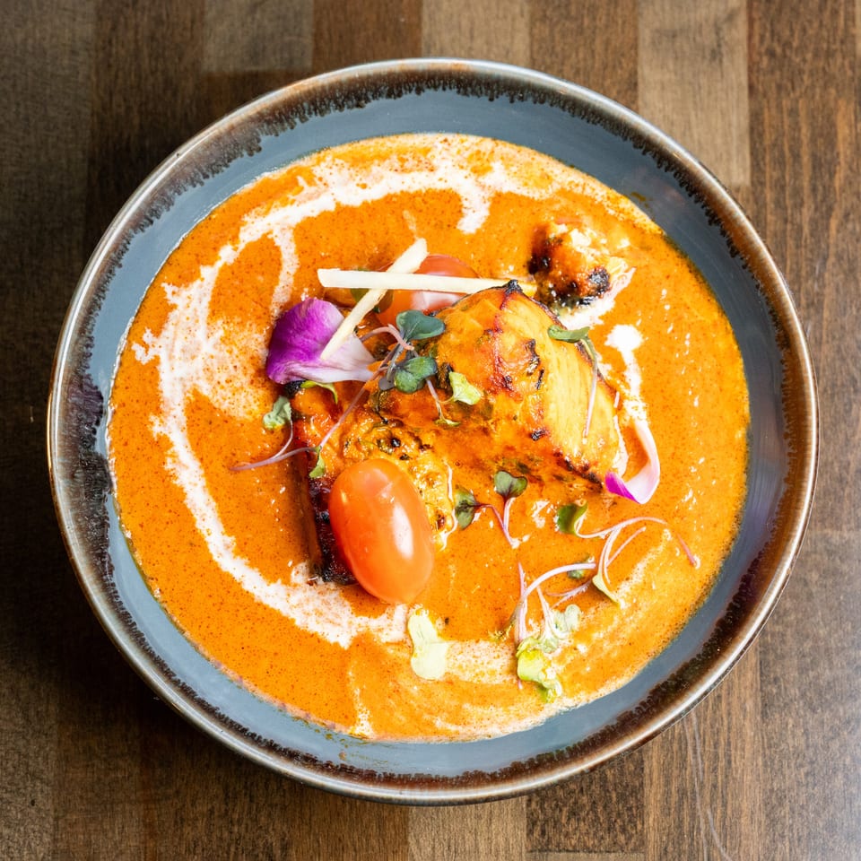 Overhead view of a vibrant orange curry dish with grilled chicken, cherry tomato, and garnishes.