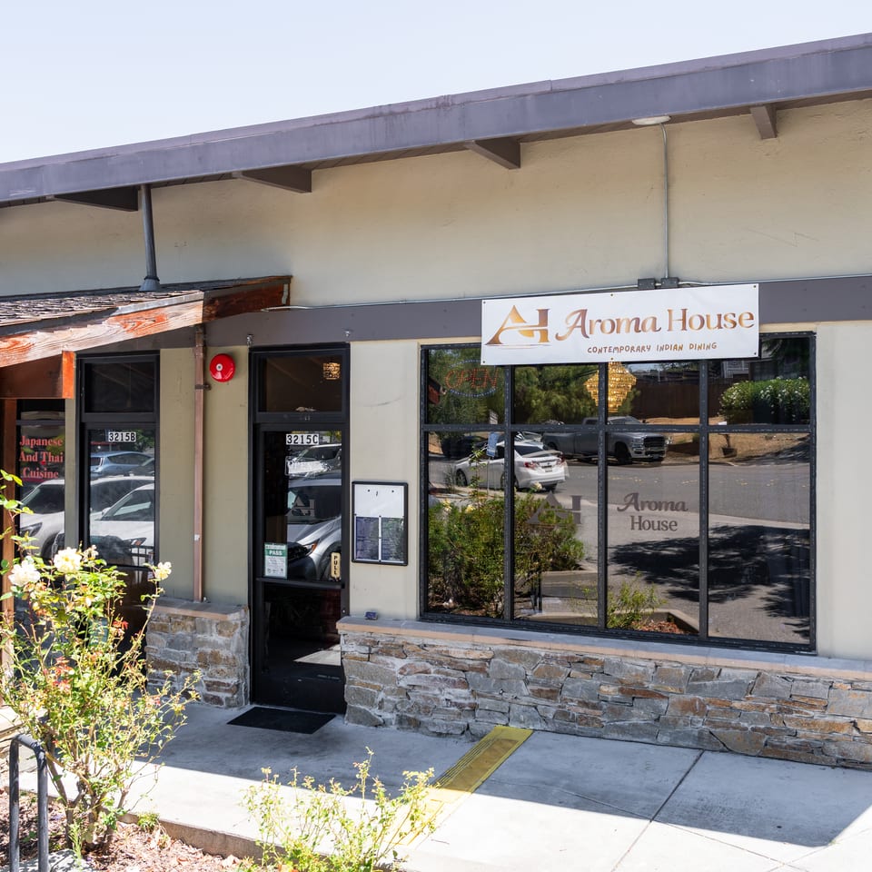 Exterior view of Aroma House, a contemporary Indian dining restaurant, with a stone facade and large windows.