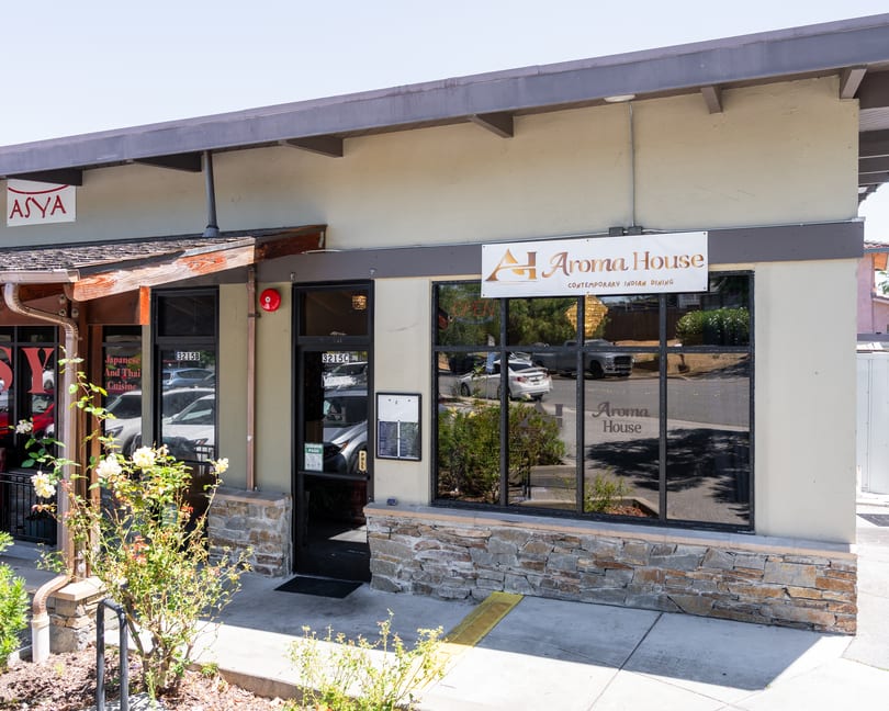 Exterior view of Aroma House, a contemporary Indian dining restaurant, with a stone facade and large windows.