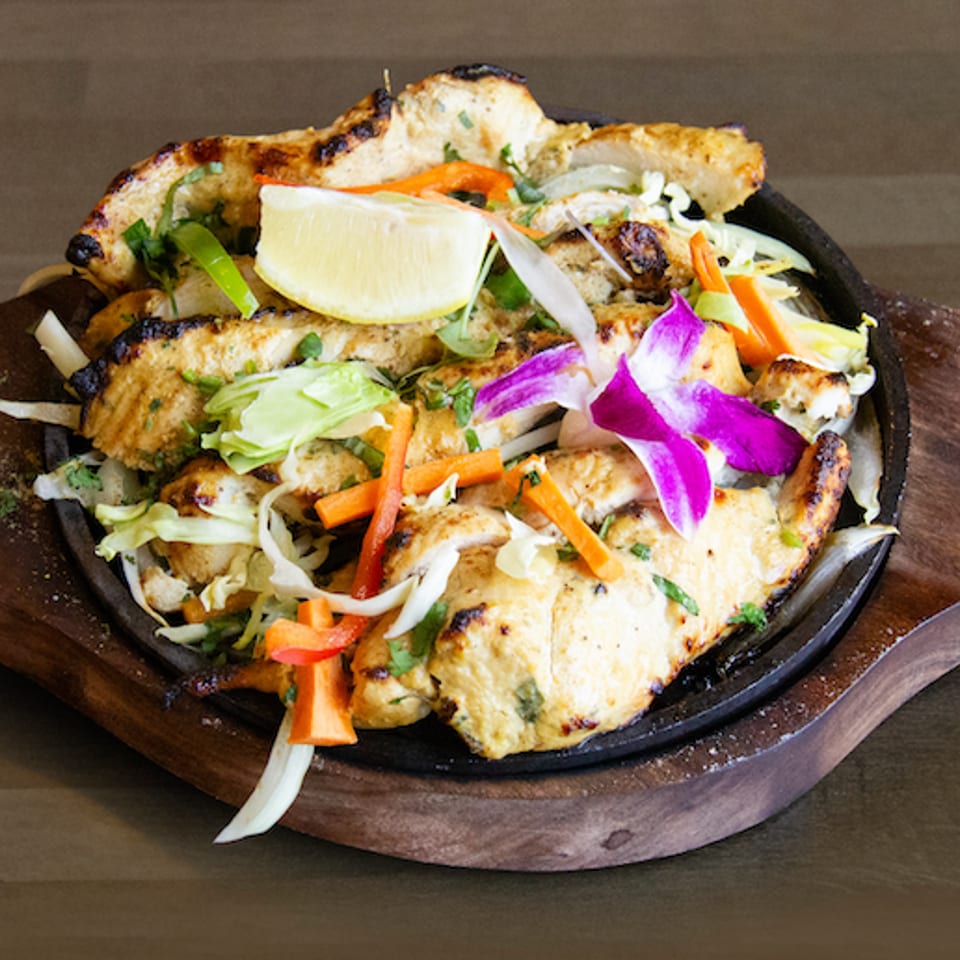 Grilled chicken strips with vegetables, a lemon wedge, and an orchid on a sizzling platter.