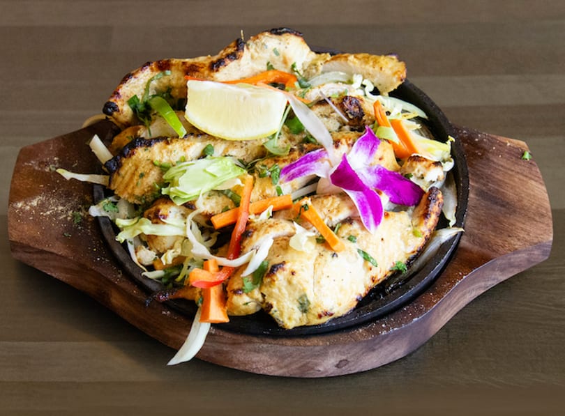 Grilled chicken strips with vegetables, a lemon wedge, and an orchid on a sizzling platter.