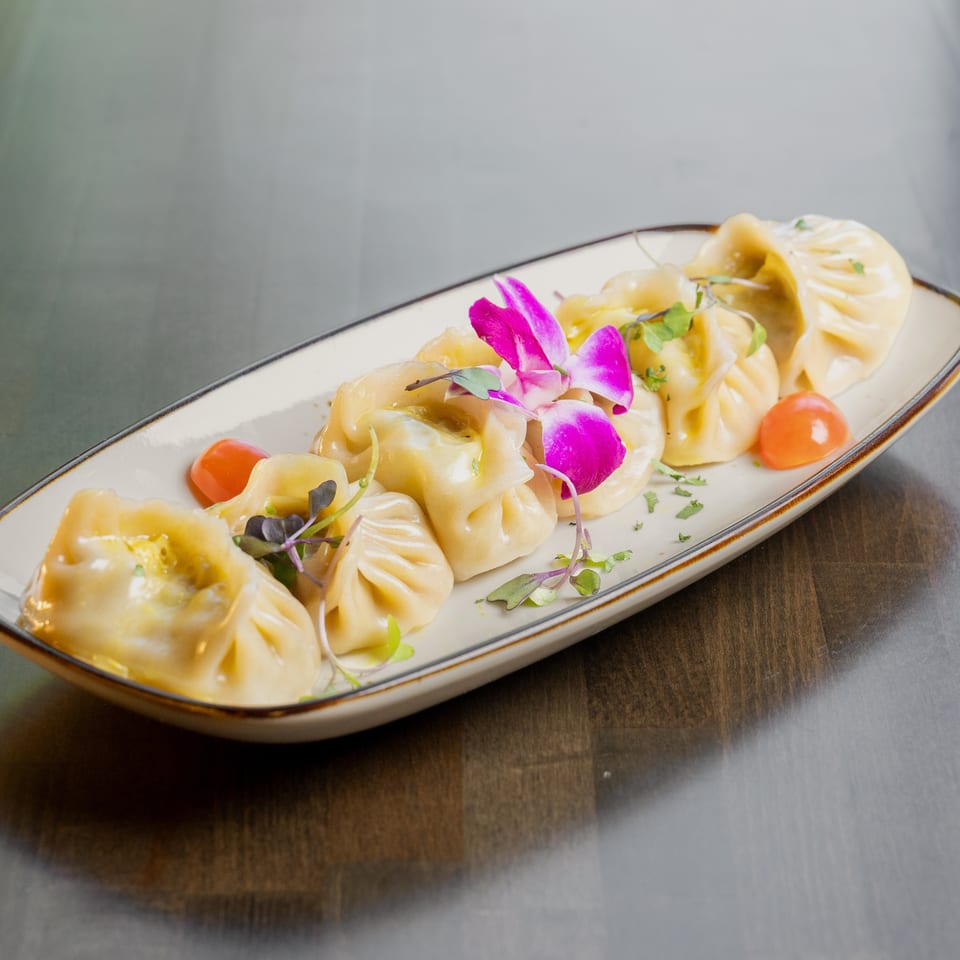A plate of steamed dumplings garnished with purple orchids, microgreens, and cherry tomatoes.
