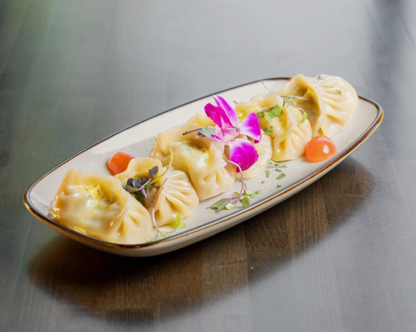 A plate of steamed dumplings garnished with purple orchids, microgreens, and cherry tomatoes.