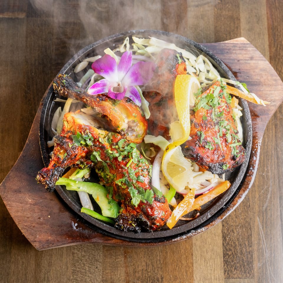 Steaming tandoori chicken with cilantro, lemon, and vegetables on a sizzling platter.