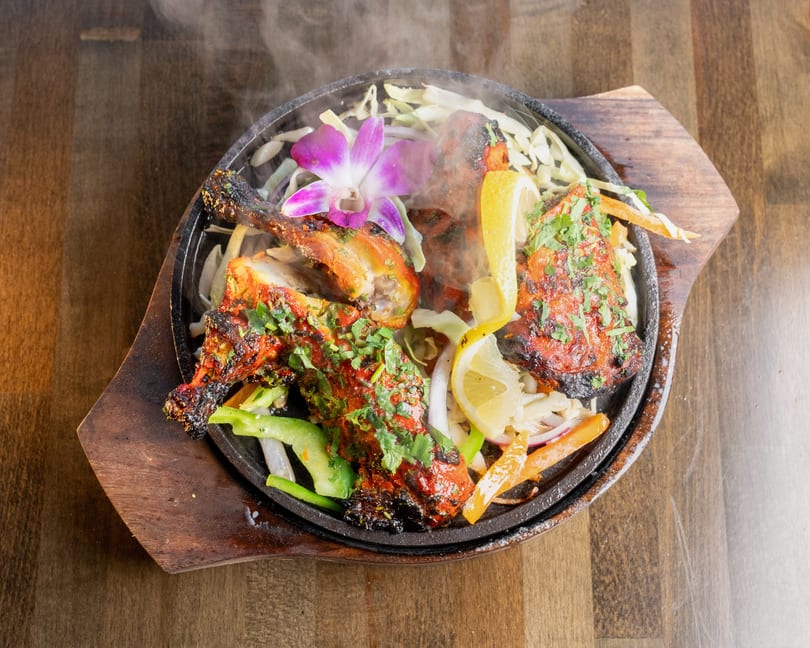 Steaming tandoori chicken with cilantro, lemon, and vegetables on a sizzling platter.