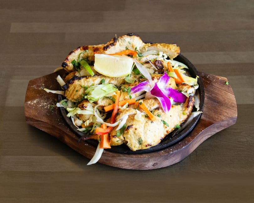 Grilled chicken strips with vegetables, a lemon wedge, and an orchid on a sizzling platter.