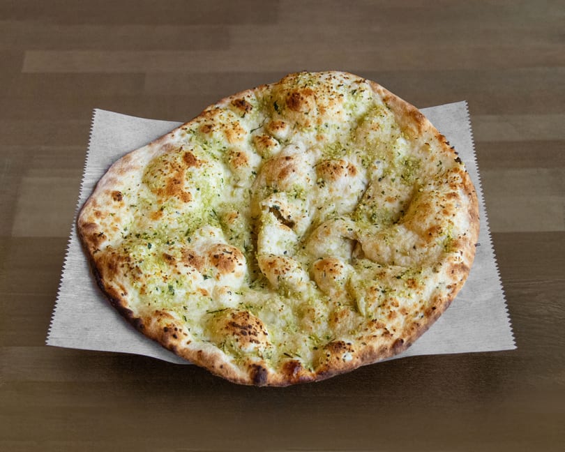 Garlic naan bread with green herbs and golden-brown crust, served on parchment paper.