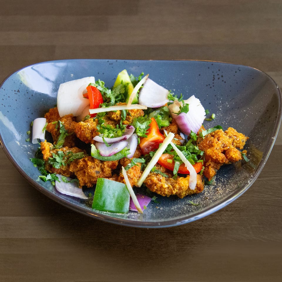 Crispy fried chicken with red and green peppers, onions, and cilantro in a blue bowl.