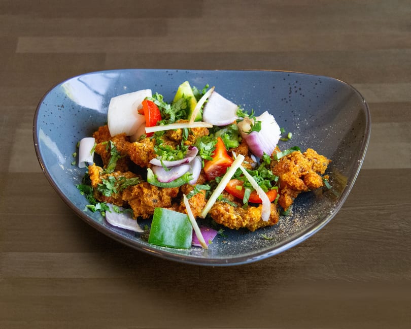 Crispy fried chicken with red and green peppers, onions, and cilantro in a blue bowl.