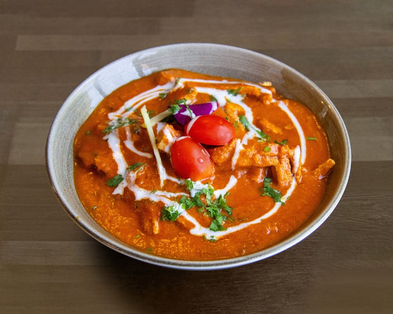 A vibrant orange curry with white cream swirls, fresh cilantro, and cherry tomatoes in a bowl.
