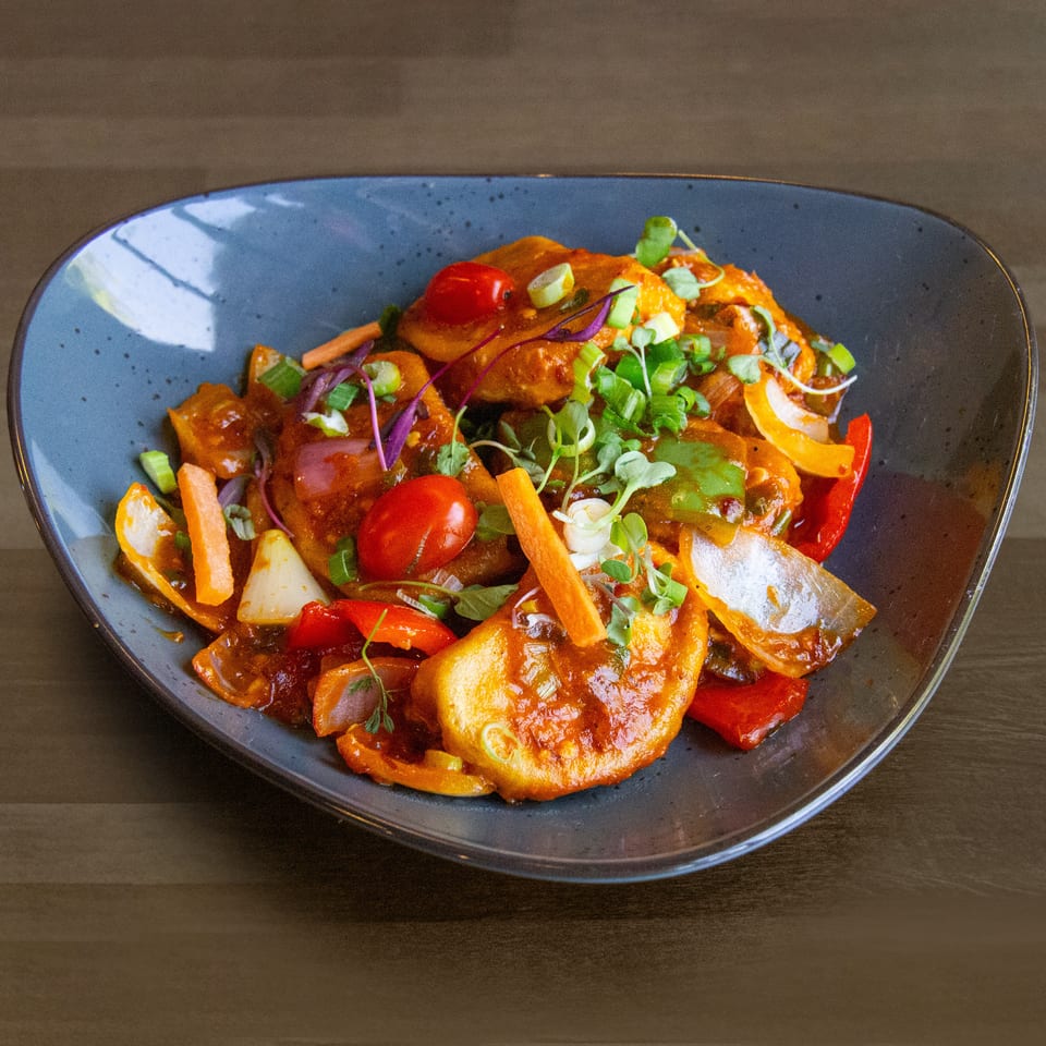 A vibrant dish of fried paneer, bell peppers, onions, and cherry tomatoes in a rich sauce.