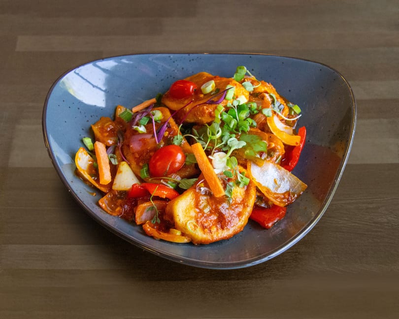 A vibrant dish of fried paneer, bell peppers, onions, and cherry tomatoes in a rich sauce.