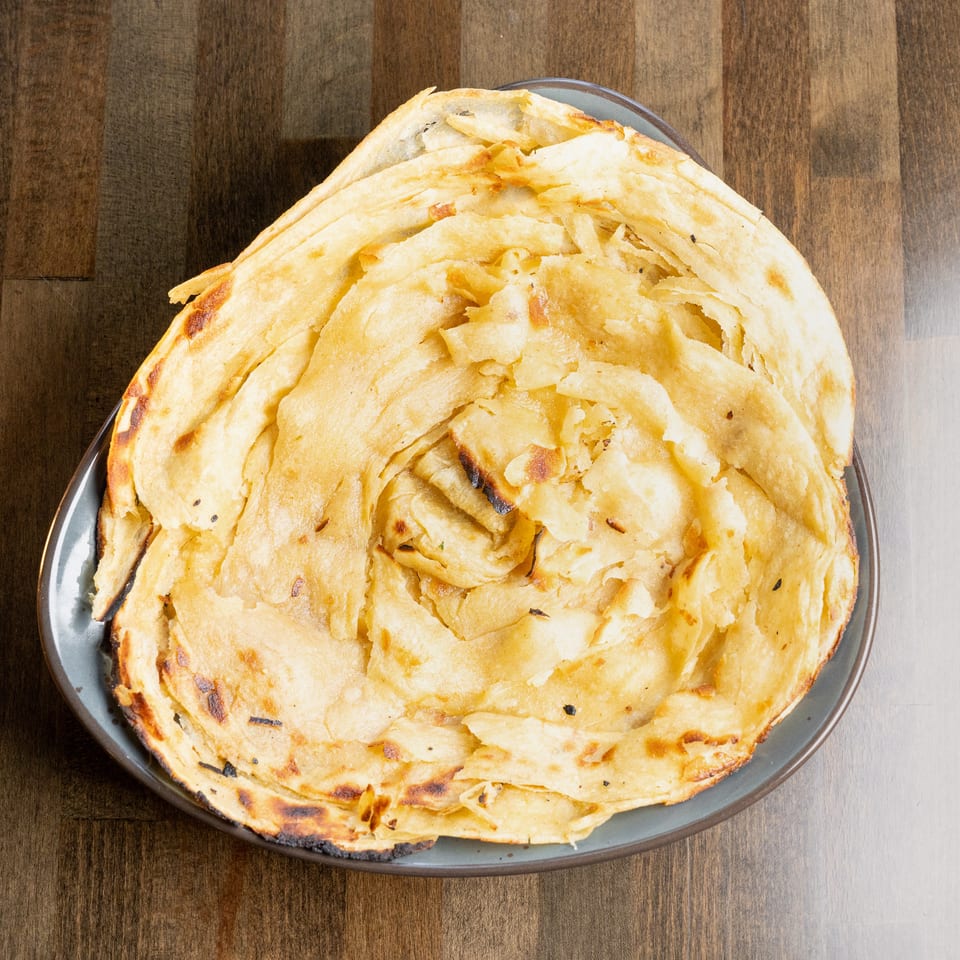 A plate of golden-brown, flaky paratha bread, lightly charred, on a wooden table.
