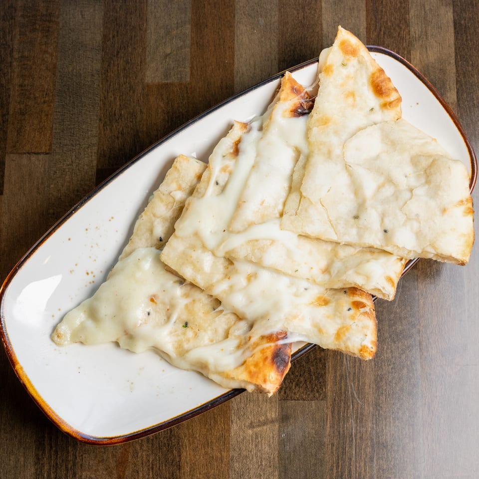 Cheesy naan bread slices on a white rectangular plate, resting on a dark wooden table.