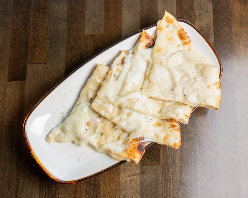Cheesy naan bread slices on a white rectangular plate, resting on a dark wooden table.