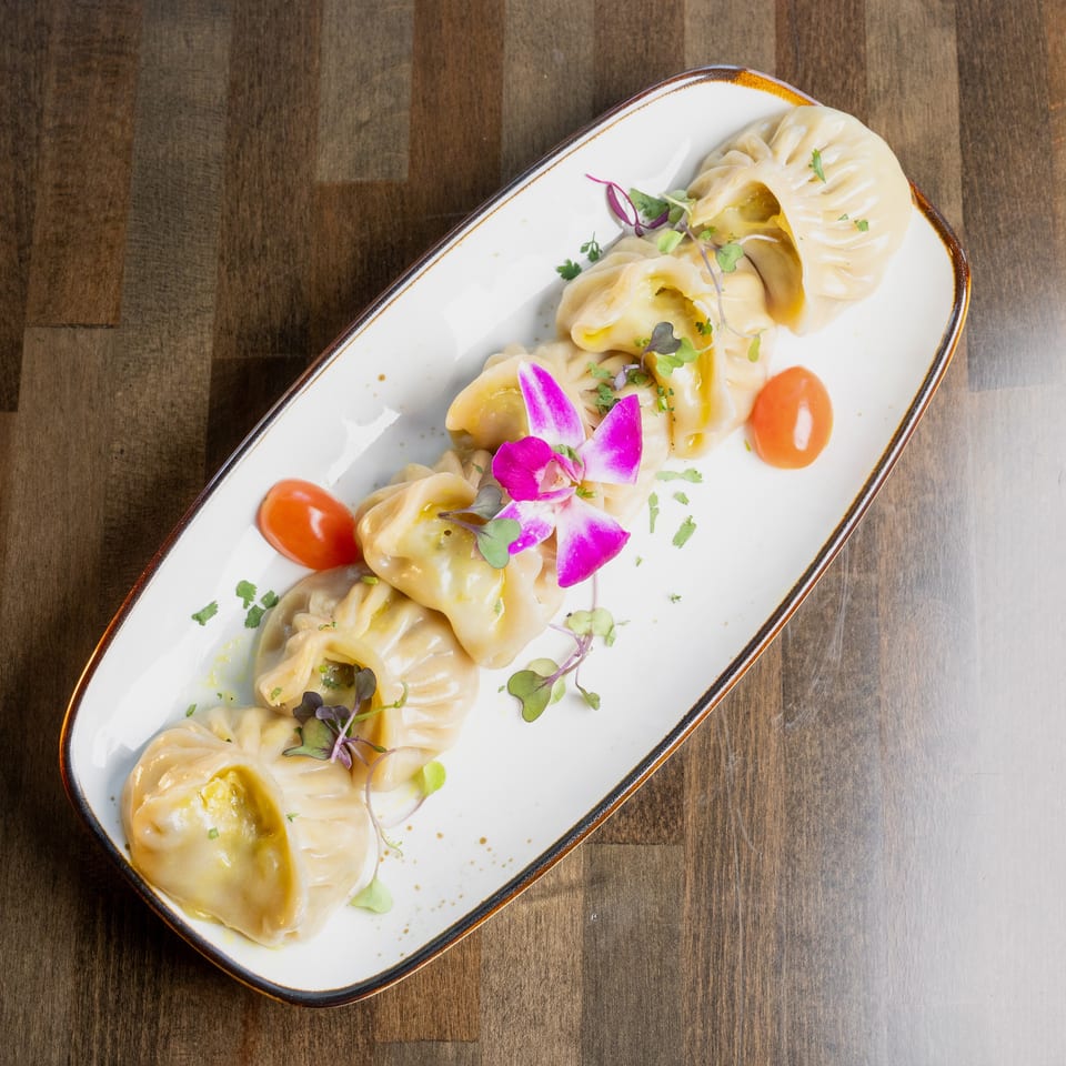 Steamed dumplings, garnished with microgreens, cherry tomatoes, and an orchid, on a white plate.