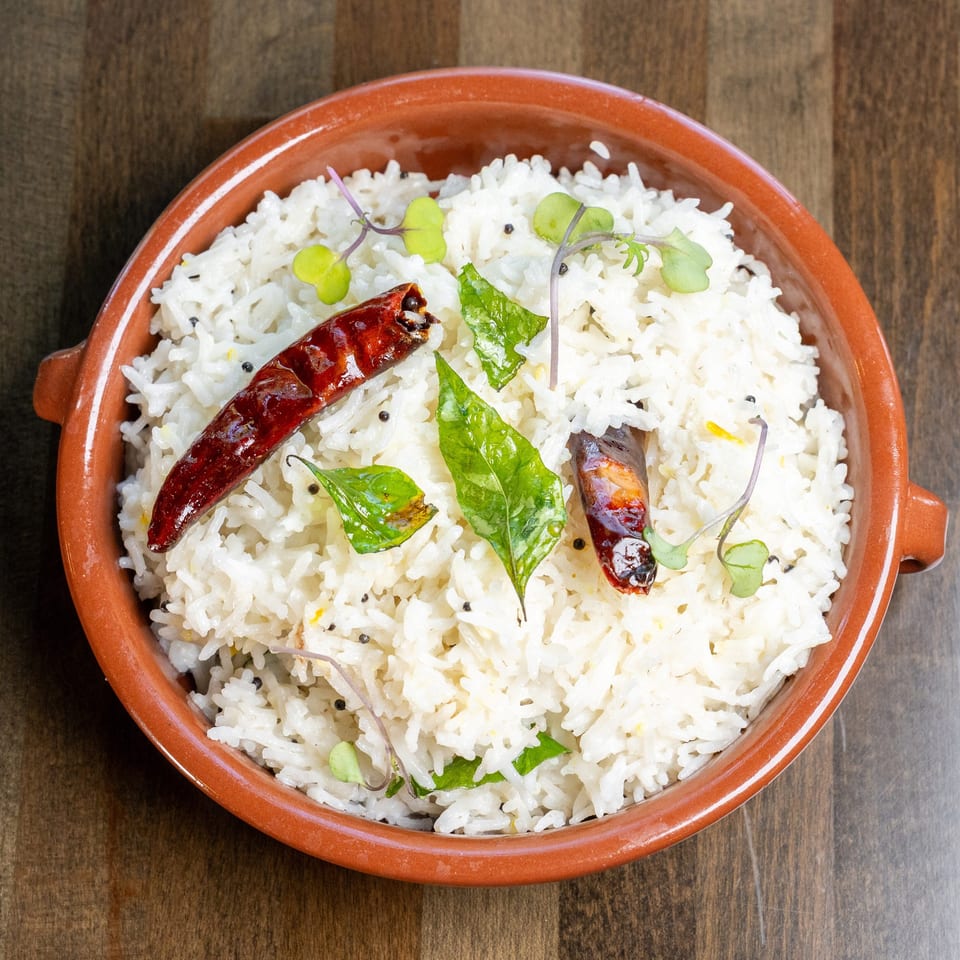 White rice in a terracotta bowl, garnished with red chilies, curry leaves, and microgreens.