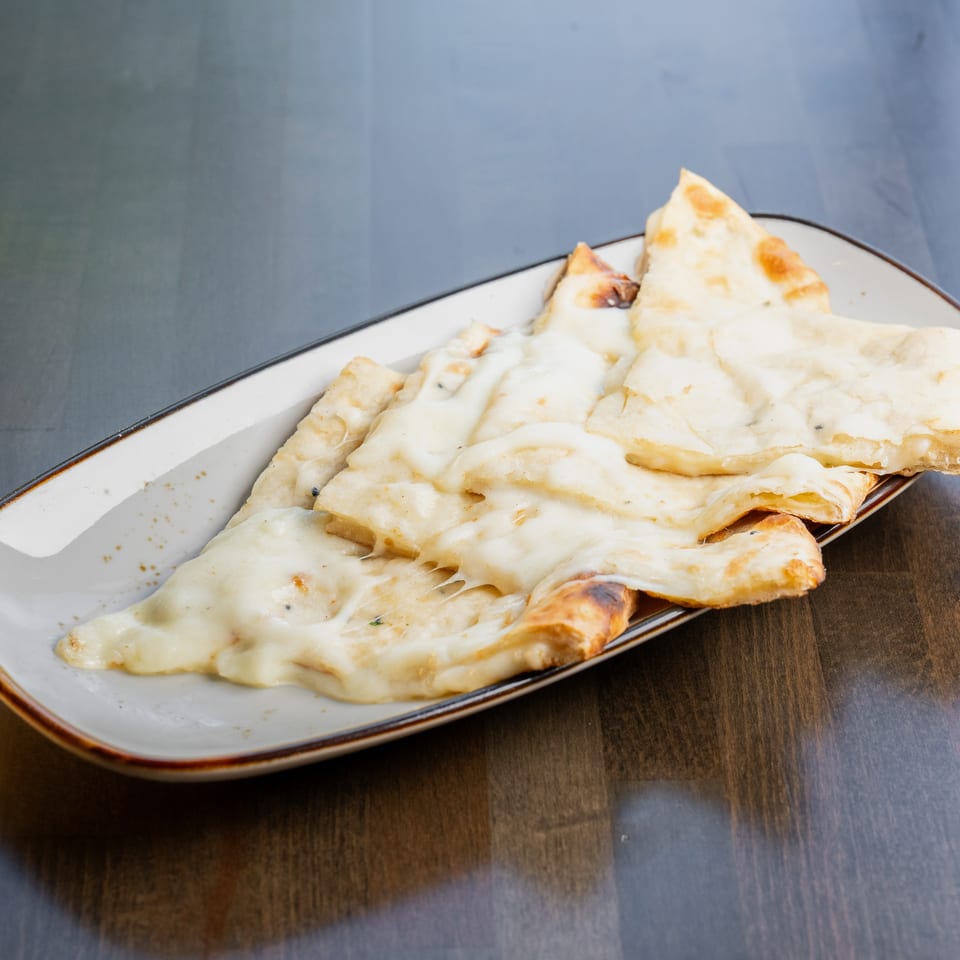 Cheesy naan bread slices, golden brown and melted, served on a rectangular white plate.