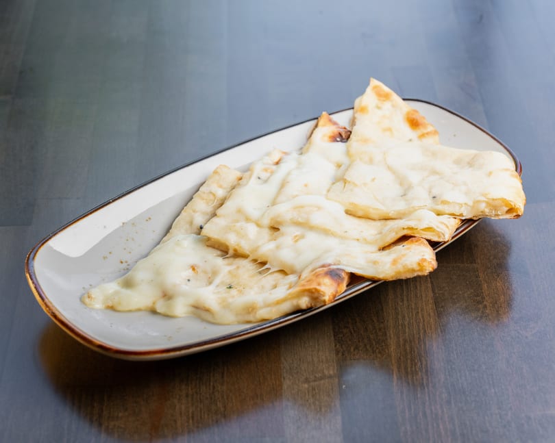 Cheesy naan bread slices, golden brown and melted, served on a rectangular white plate.