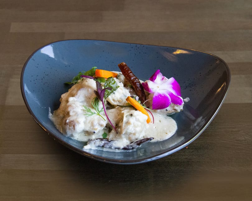 Creamy chicken dish garnished with herbs, carrots, dried chili, and an orchid in a blue bowl.