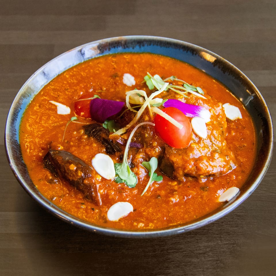 Rich orange curry with meat, garnished with cherry tomatoes, microgreens, and sliced almonds.