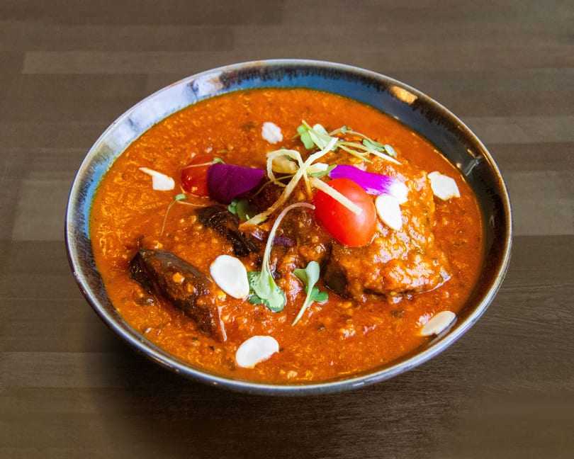 Rich orange curry with meat, garnished with cherry tomatoes, microgreens, and sliced almonds.