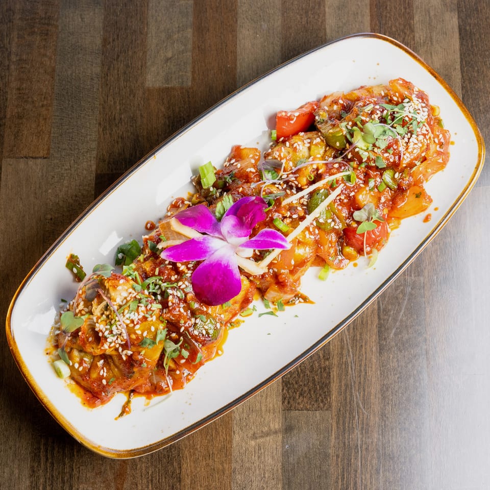 A long white plate of chili paneer, garnished with sesame seeds, cilantro, and an orchid.