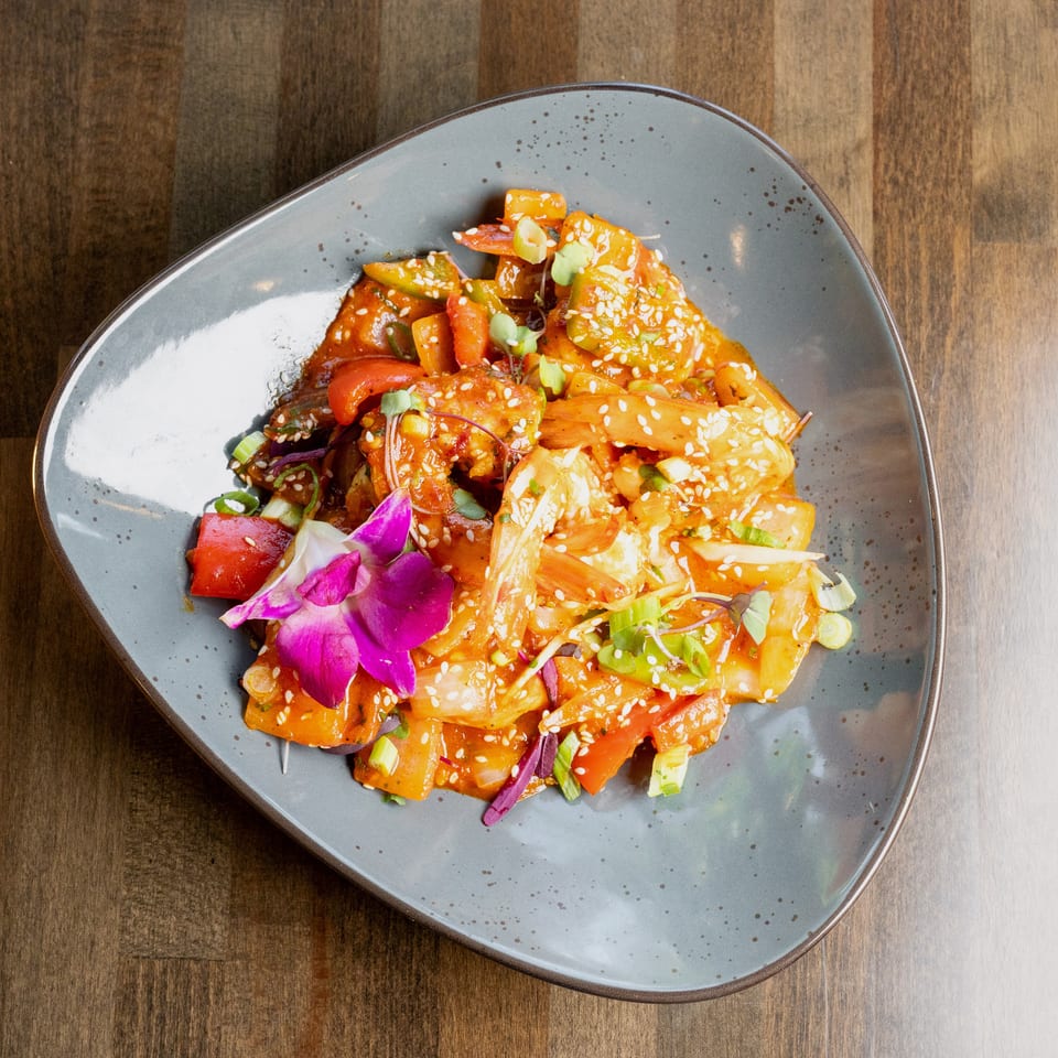 Sweet and sour shrimp with peppers, onions, and sesame seeds, garnished with an orchid.