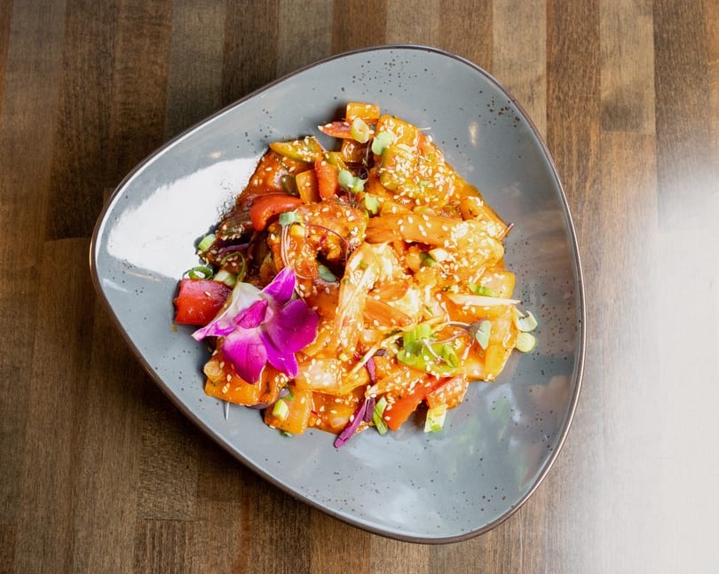 Sweet and sour shrimp with peppers, onions, and sesame seeds, garnished with an orchid.