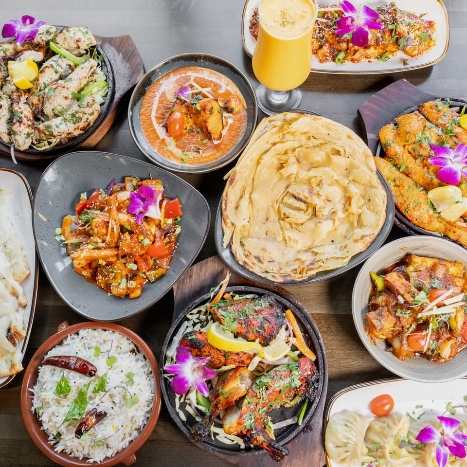 An overhead shot of a feast of Indian dishes, including curries, naan, rice, and grilled meats.