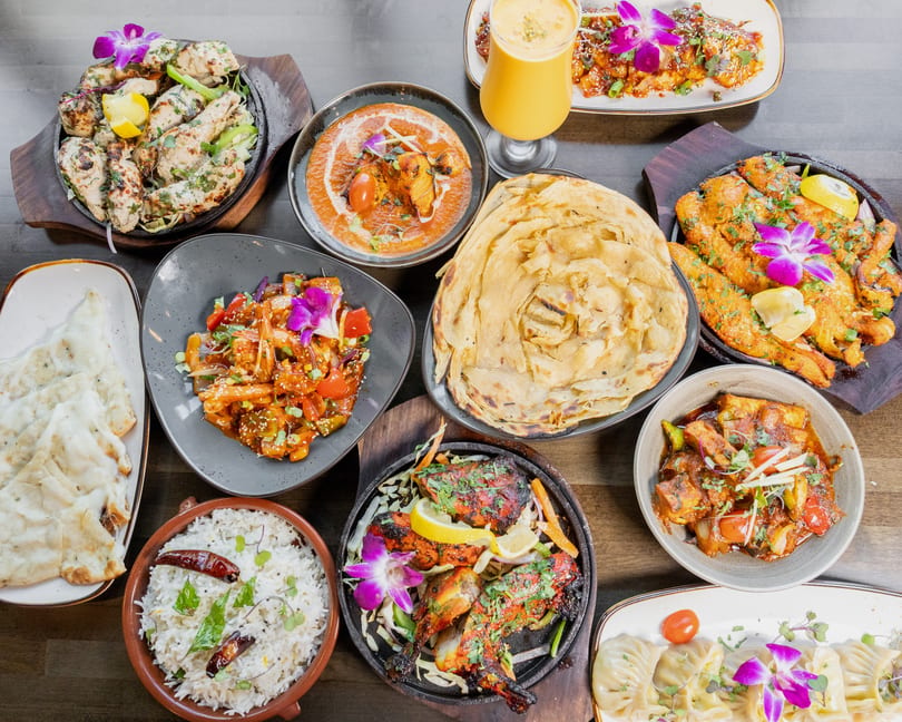 An overhead shot of a feast of Indian dishes, including curries, naan, rice, and grilled meats.