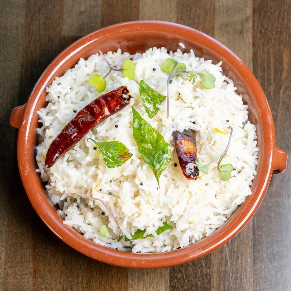 White rice in a terracotta bowl, garnished with dried red chilies, curry leaves, and microgreens.