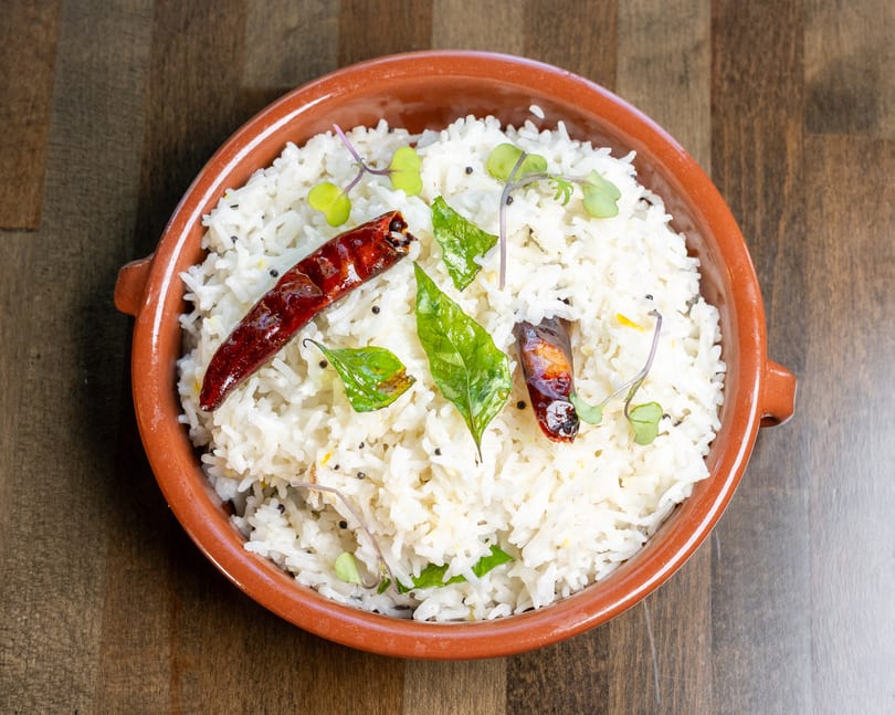 White rice in a terracotta bowl, garnished with dried red chilies, curry leaves, and microgreens.